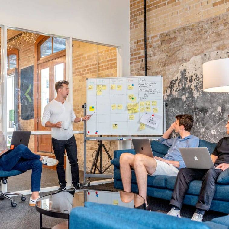 Man by a whiteboard calendar of ideas discussing them with other team members